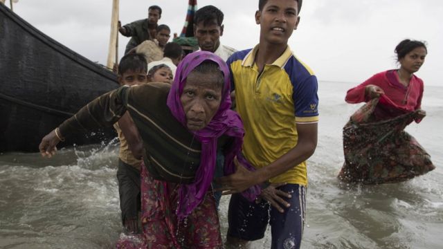 A young Rohingya man carries an elderly woman, after the wooden boat they were travelling on from Myanmar crashed into the shore and tipped everyone out in Dakhinpara, Bangladesh