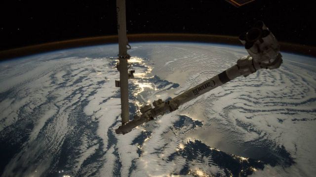 Imagem mostrando um braço mecânico no espaço, sobre a atmosfera da Terra
