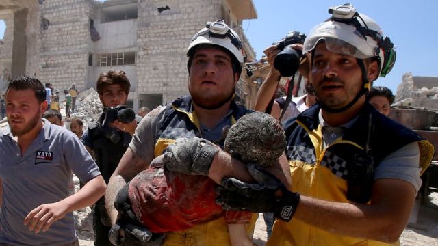 Membros da defesa síria, conhecidos como capacetes brancos, retiram uma criança ferida debaixo de escombros depois de um ataque russo na província de Idlib em julho de 2019