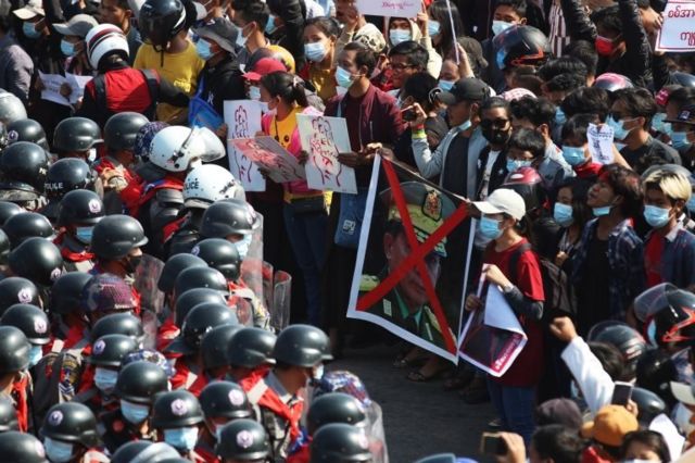 Demonstrators hold up a sign showing a crossed out picture of military junta chief General Min Aung Hlaing as they face riot police during a protest against the military coup in Naypyitaw, Myanmar, 08 February 2021