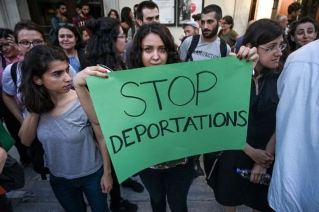 'Sınırdışı etmelere son" yazılı pankart tutan bir kadın