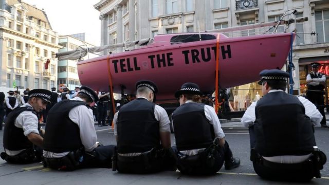 Полицейские силят рядом с розовым катером, который протестующие установили на перекрестке. На борту написано: "Скажите правду"