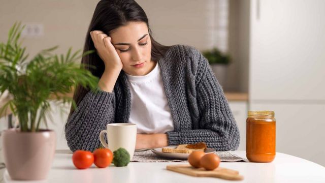 Young woman looks unhappily at food on her plate