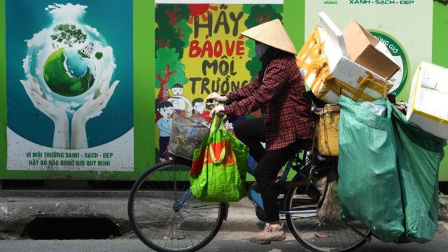 A scrap vendor rides a bicycle past a billboard that reads "Let's Protect the Environment" in Hanoi