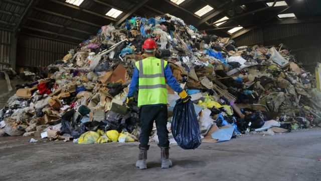 Man carrying trash in front of piles of plastic