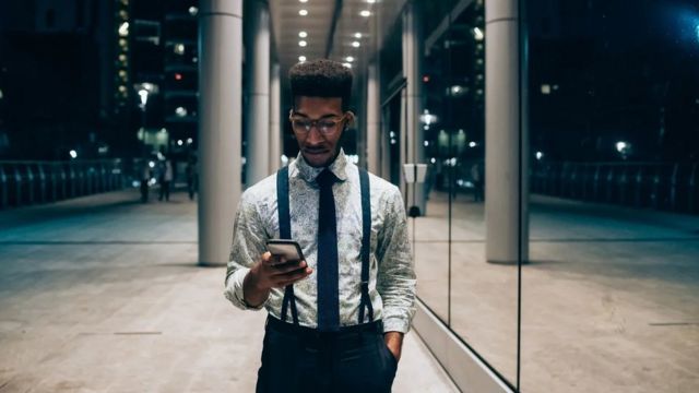 Homem de gravata e suspensórios olhando um celular