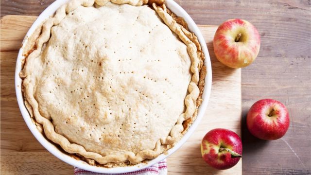 Яблочный пирог на деревянной доске и яблоки справа