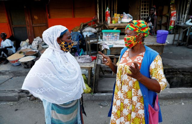 Two African women in colourful face masks speaking to each other on the street.
