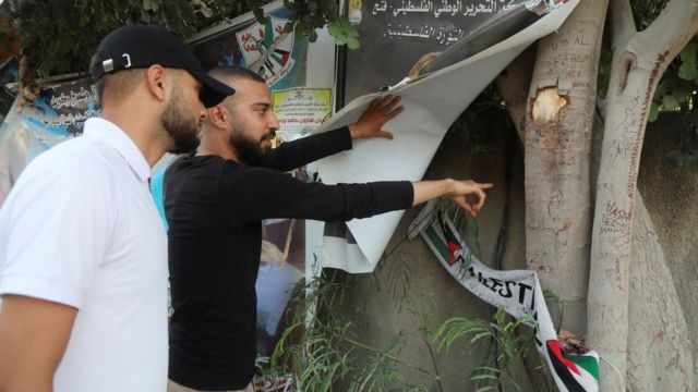 فلسطينيان ينظران إلى آثار الرصاص على جذع شجرة في مدينة جنين بالضفة الغربية، بجوار مكان إطلاق النار على شيرين أبو عاقلة (3 يوليو / تموز 2022)