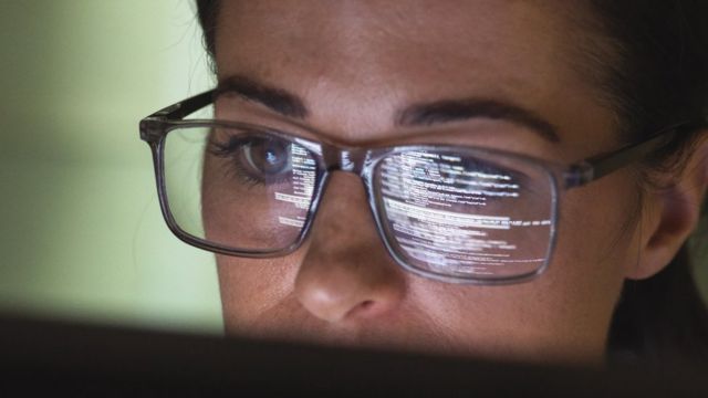 女性のかけている眼鏡にコンピューターのモニターが反射している写真
