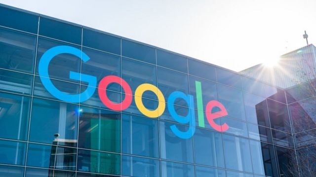Foto da sede do Google, um prédio de vidro sob o sol com o logo da empresa escrito em letras coloridas