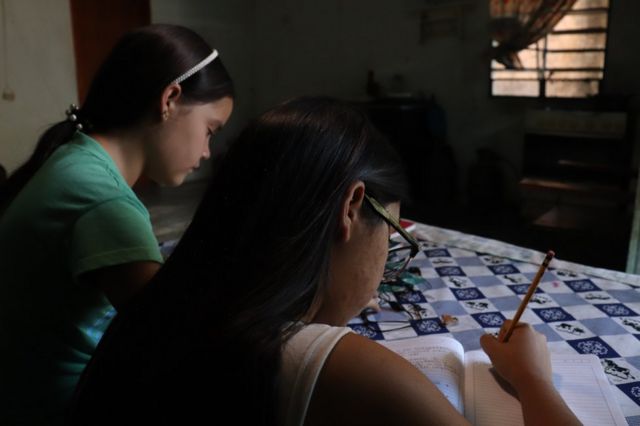 Valeria Torres writing on a notebook, with a student next to her