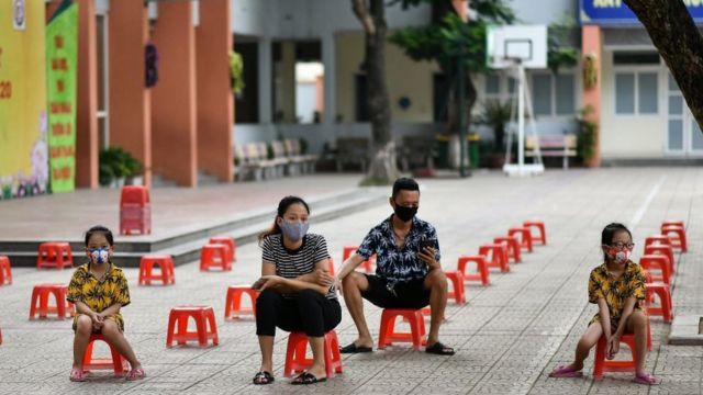 A family sit on plastic stools as they wait to be tested at a makeshift rapid testing centre as Vietnam records a rise in cases of the COVID-19 coronavirus in Hanoi on July 31, 2020.