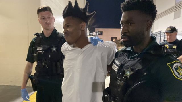 Dos policías sostienen a Keith Melvin Moses, de 19 años, vestido de blanco y esposado