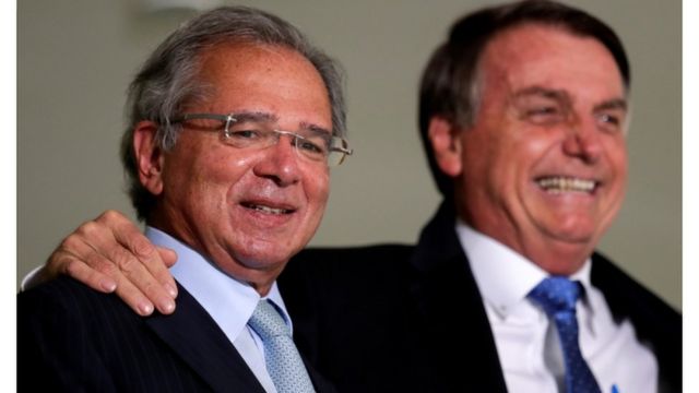 Paulo Guedes e Jair Bolsonaro abraçados e sorrindo