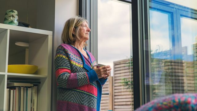 mulher idosa olha para o horizonte próxima à janela