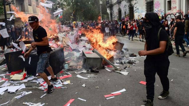 Jóvenes manifestantes prenden fuego a una pila en medio de la calle.