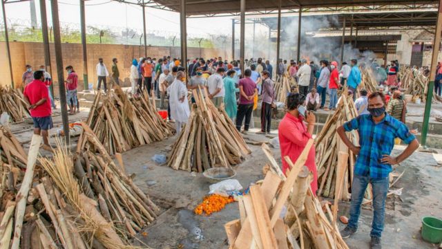 People perform the last rites for relatives who died of Covid-19 disease as other funeral pyres are seen during a mass cremation at Ghaziapur Municipal crematorium.