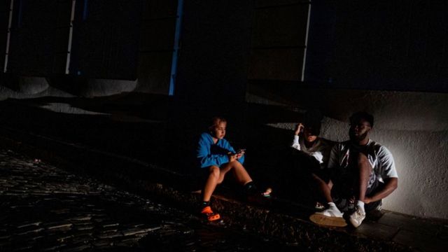 Personas en una acera en San Juan una noche sin servicio eléctrico