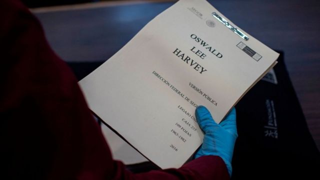Unas manos enguantadas sostienen un reporte titulado 'Lee Harvey Oswald'