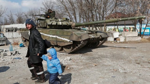 A man and is child walk past a tank belonging to pro-Russian separatists