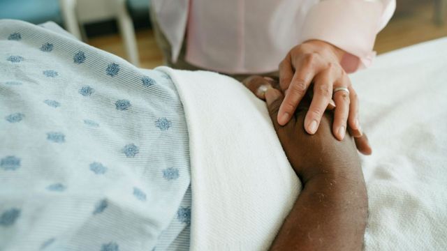 Mulher segurando a mão de pessoa hospitalizada