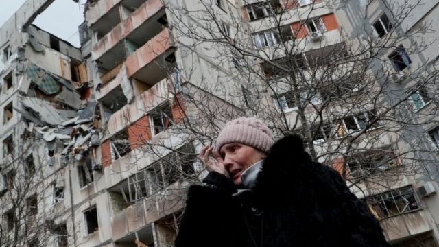 Una donna davanti a un edificio distrutto a Mariupol