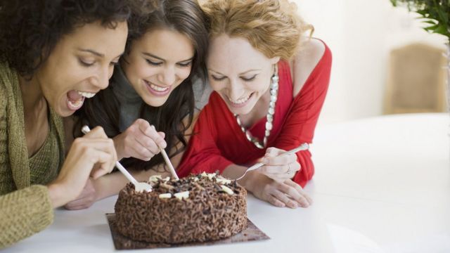 Tre mujeres ríen a punto de comer una torta de chocolate
