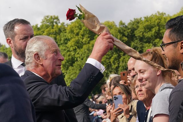El rey Carlos III recibe una rosa al saludar en su llegada a Buckingham Palace.