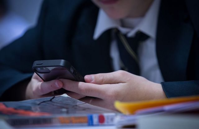 Estudiante con celular en un aula en Reino Unido
