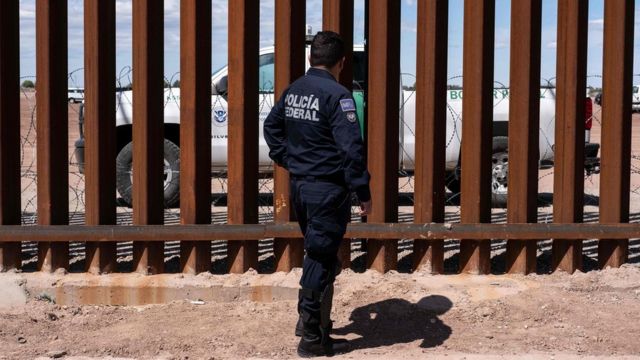 Un policía federal de México observa a través de la barrera fronteriza a una patrulla fronteriza de EE.UU.