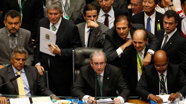 Eduardo Cunha na mesa da Câmara dos Deputados, rodeado por parlamentares homens