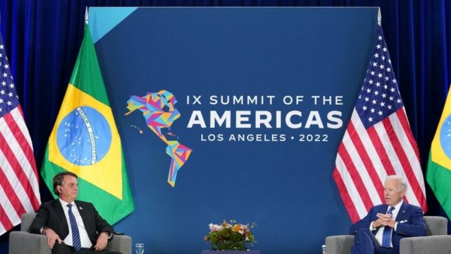 Bolsonaro e Biden sentados, com bandeiras e telão com logo da Cúpula das Américas atrás
