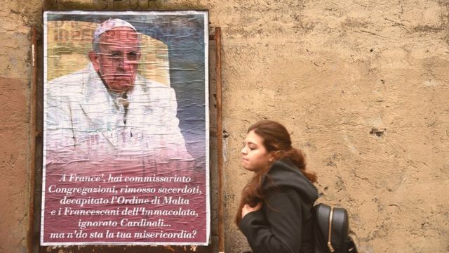 Woman walking past a poster of Pope Francis