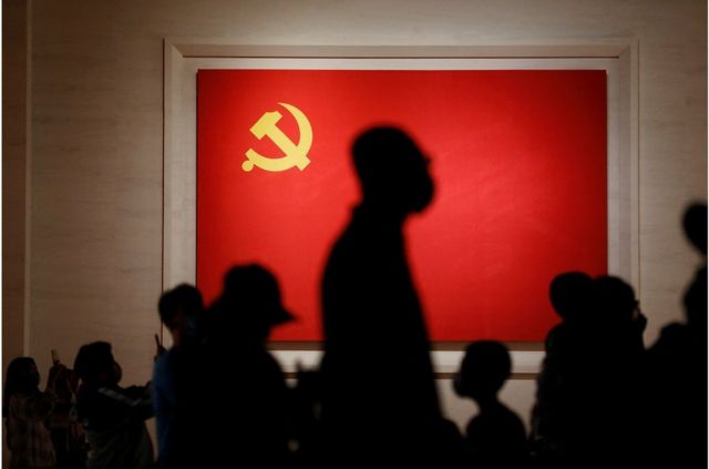 Silhouettes of tourists in front of the Chinese Communist Party flag on display at the Chinese Communist Party Museum in Beijing.