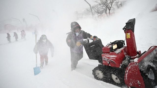 Crew members push a snow cleaning machine