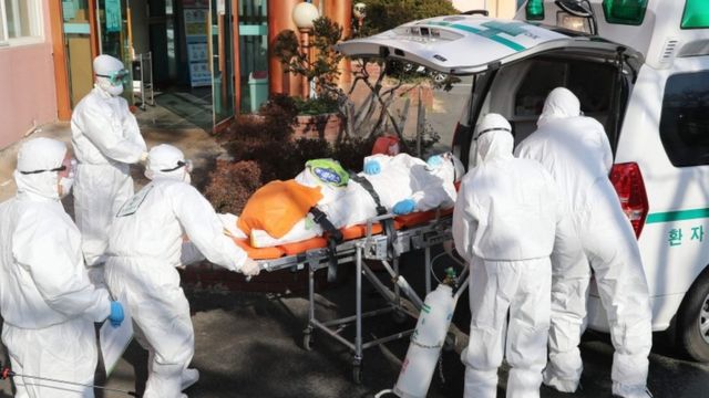 Trabajadores de la salud en trajes protectores trasladan a un paciente de coronavirus en una camilla en Daegu, Corea del Sur