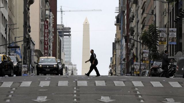 Un hombre cruza la calle con el Obelisco de fondo.