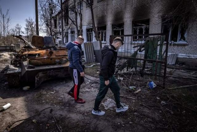 Men walk around a burnt armoured vehicle near a damaged school in Bohdanivka village, northeast of Kyiv