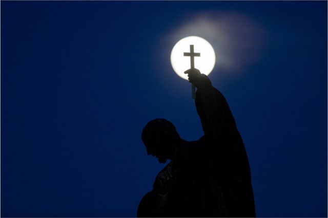 The pink supermoon rises behind a statue on Charles Bridge in Prague, Czech Republic
