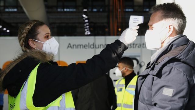 متطوعة تتحقق من درجة حرارة ضابط شرطة في نقطة 4 بمطار تمبلهوف السابق في برلين