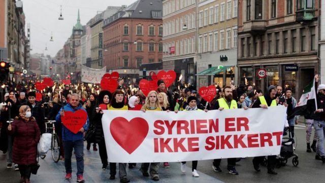 بعد إلغاء تصاريح إقامة مئات السوريين، متظاهرون في كوبنهاغن ينظمون لافتة كتب عليها "سوريا ليست آمنة" .