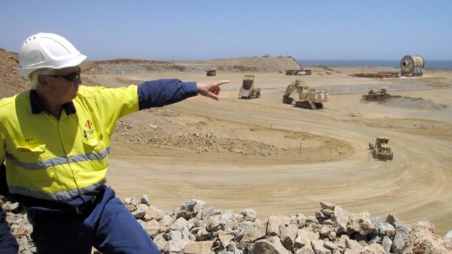 A man pointing across an iron ore mine