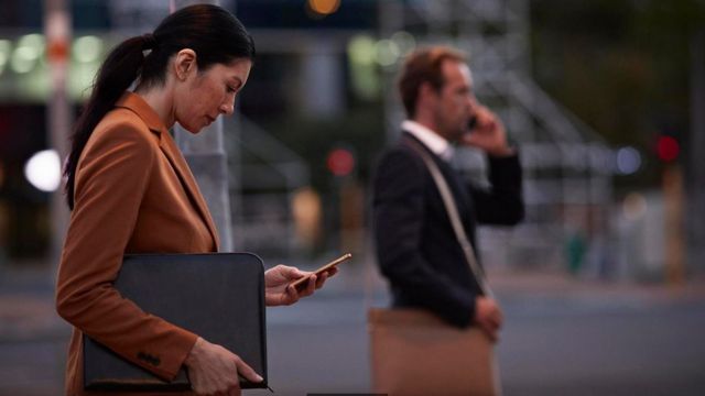 Dos personas vestidas con traje cruzando una calle, con sus teléfonos en la mano