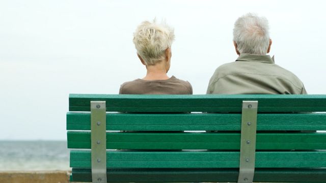 Un hombre y una mujer de espaldas sentados en un banco frente al mar