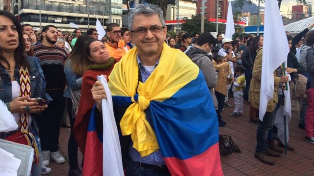 Fernando Rincón sostiene una bandera blanca mientras está envuelto con una colombiana.