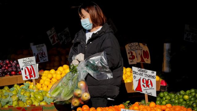 A woman wears a mask and gloves as he shops at a fruit stand