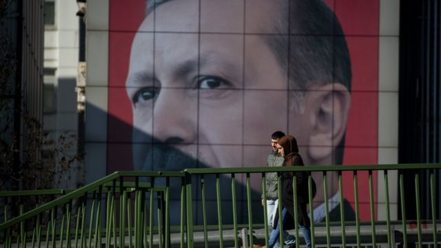 Una pareja camina frente a un gigantesco letrero con la imagen de Erdogan.