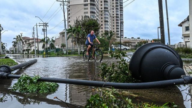 Homem passando de bicicleta em meio a destroços causados pelo furacão na Flórida