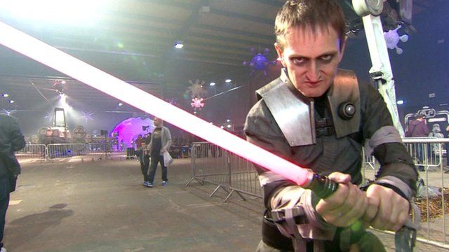 A man wearing a Star Wars outfit wields a toy light sabre